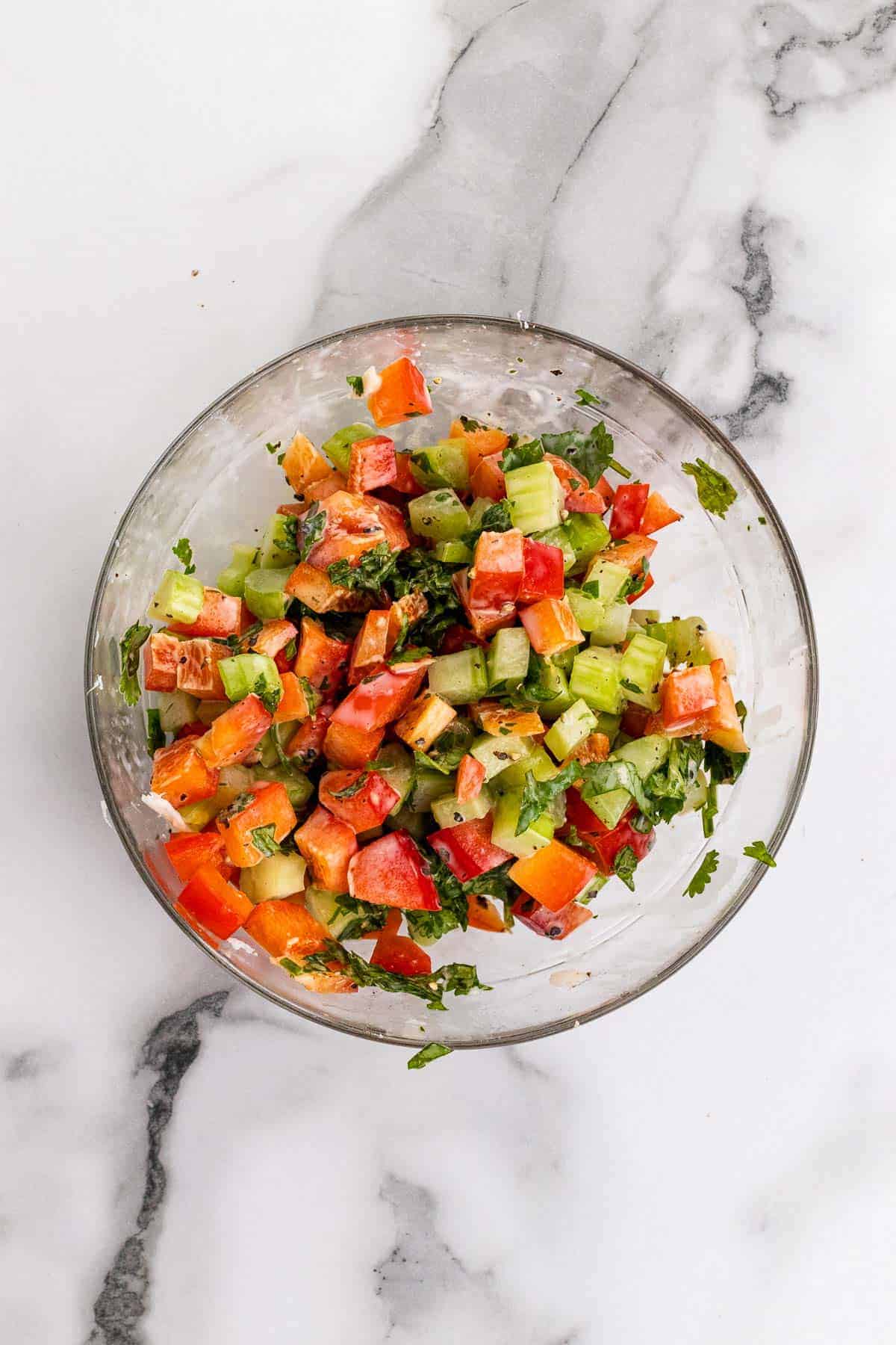 Bell peppers, celery, cilantro, salt, and dressing mixed together in a glass bowl, as seen from above