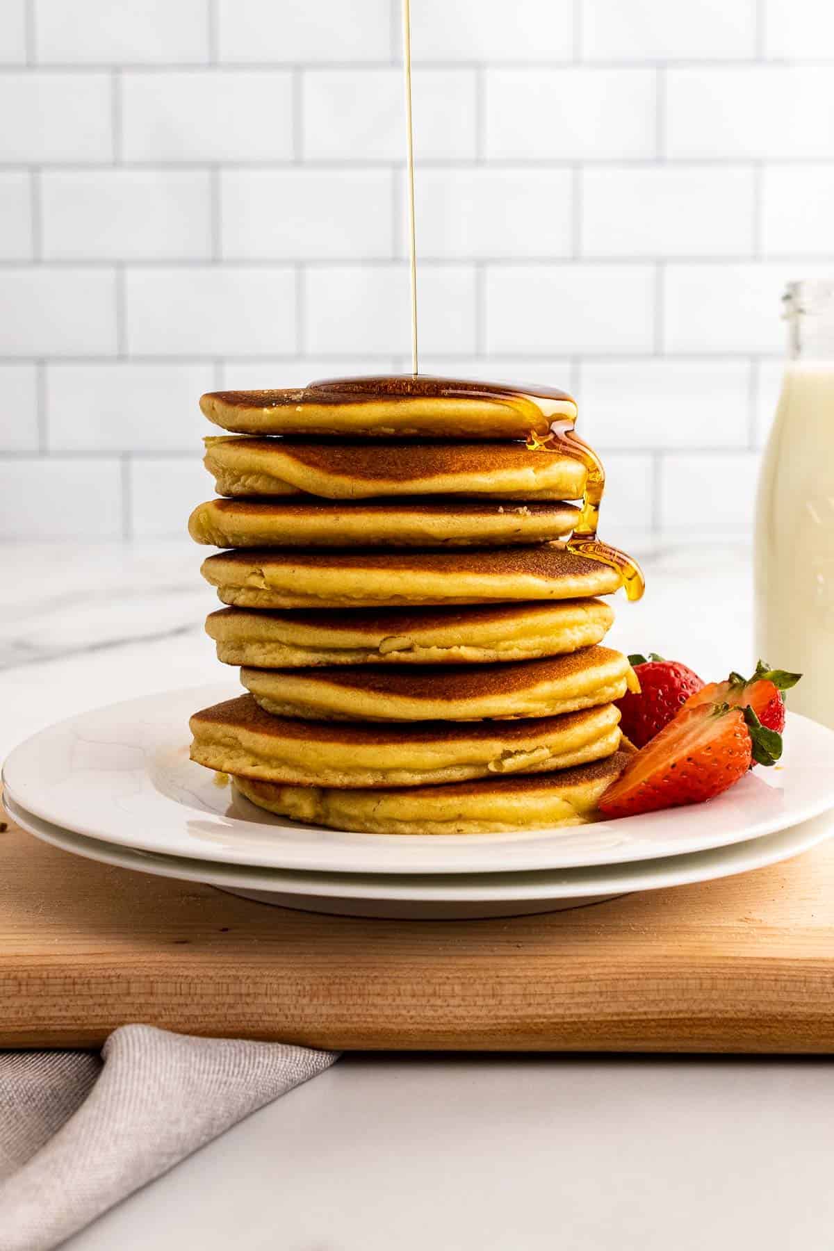 Stack of diabetes friendly pancakes with almond flour on a plate with strawberries, syrup being poured on top