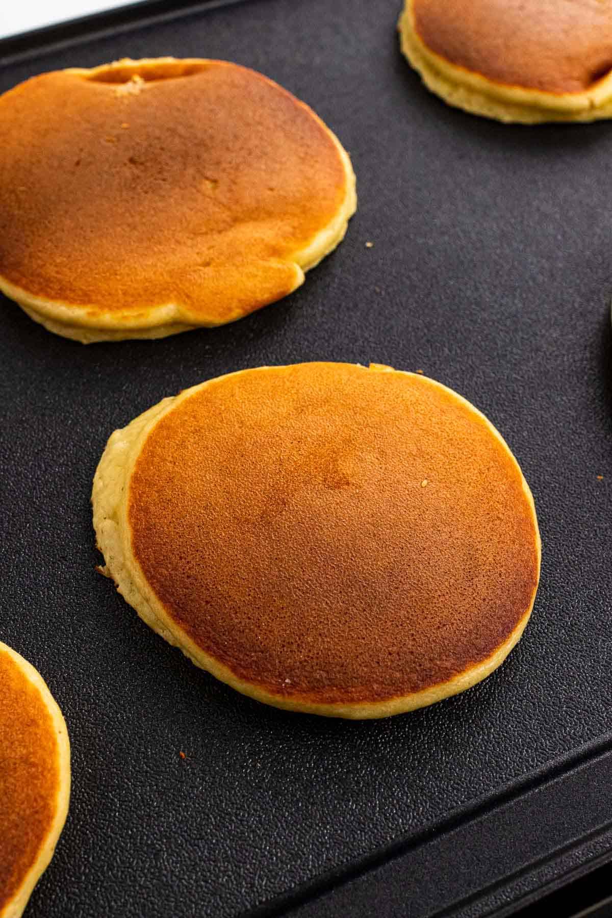 Four pancakes cooking on a griddle, flipped once