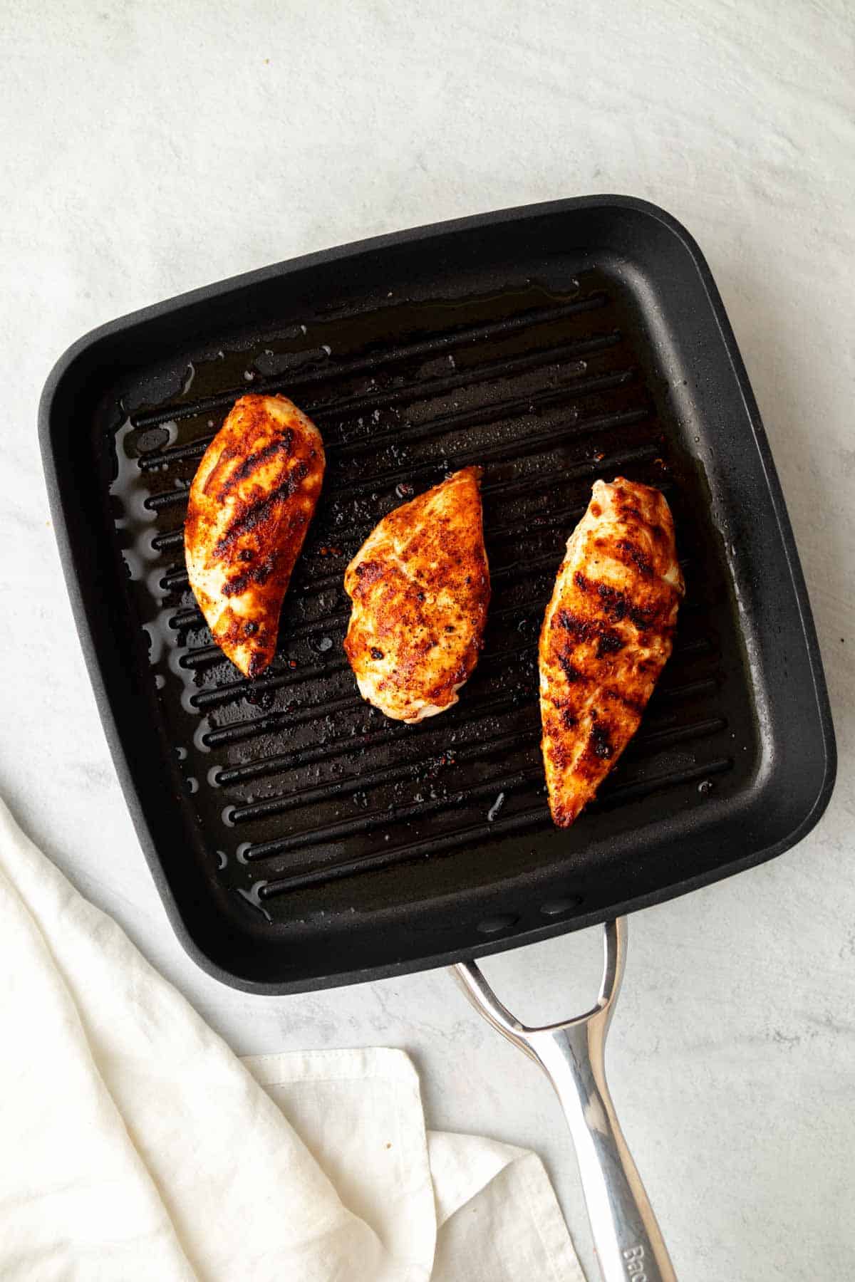 Three chicken breasts cooking on a grill pan, as seen from above