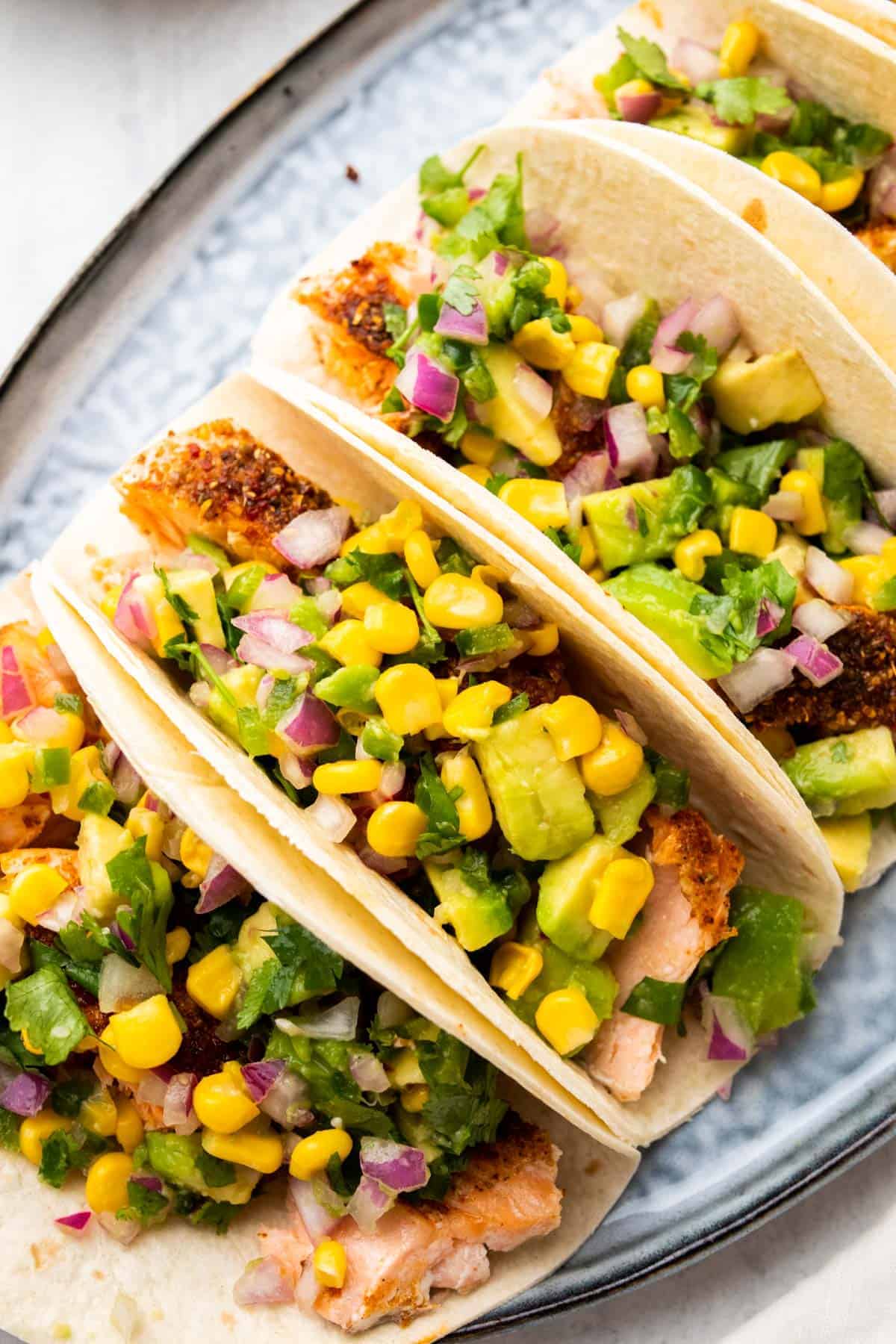 Close up of tacos on a serving tray topped with corn avocado salsa