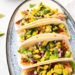 Close up of multiple tacos lined up in a row on a decorative serving tray