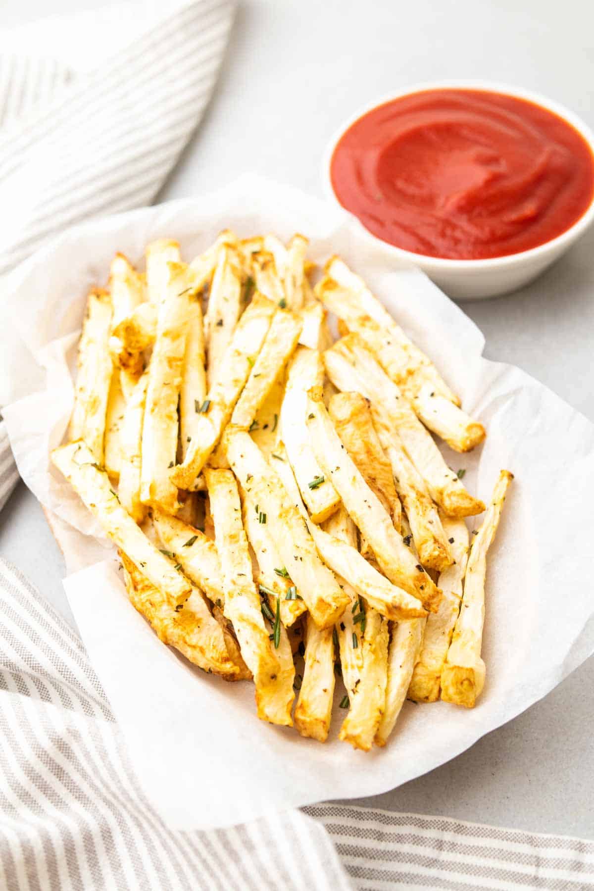 Close-up of celery root fries in a basket next to a ramekin of ketchup