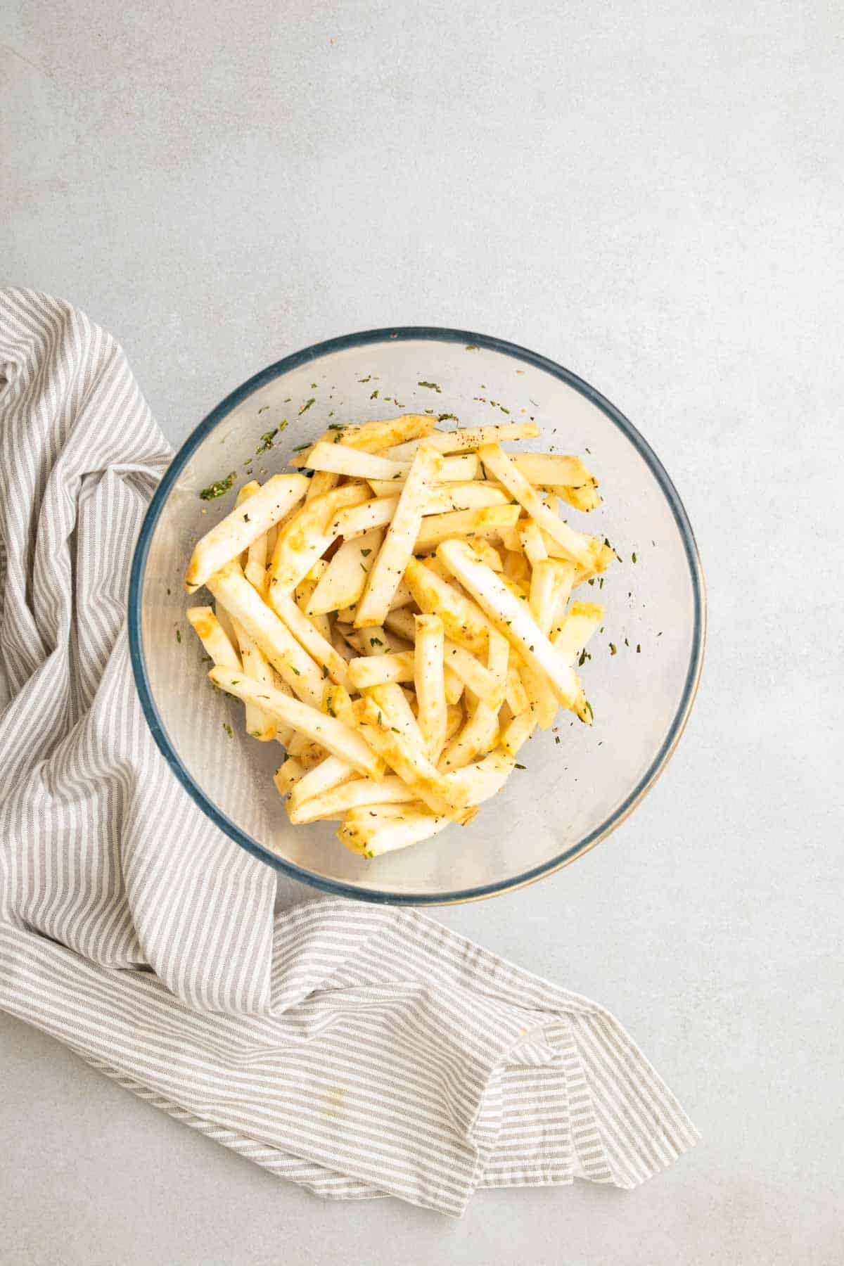 Fries tossed in oil and rosemary in a glass bowl, as seen from above
