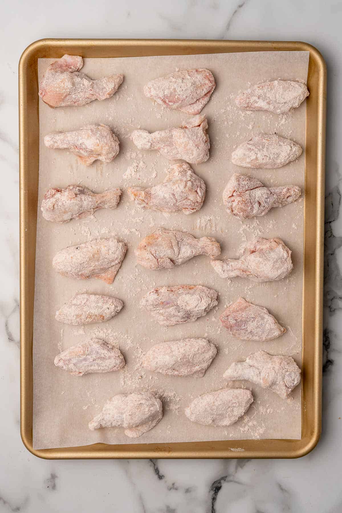 Wings coated in flour and spices on a baking sheet