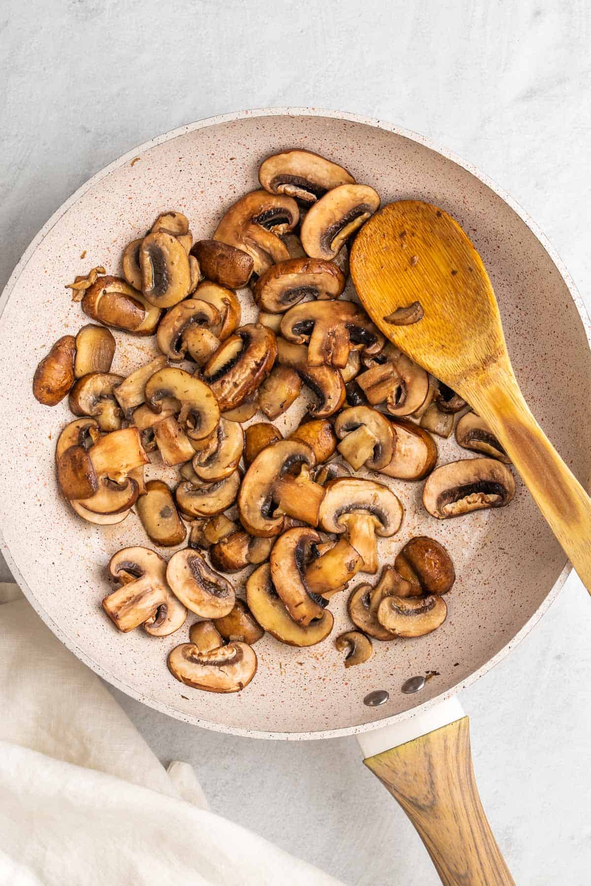 Mushrooms cooking in a pan with a wooden spoon, as seen from above