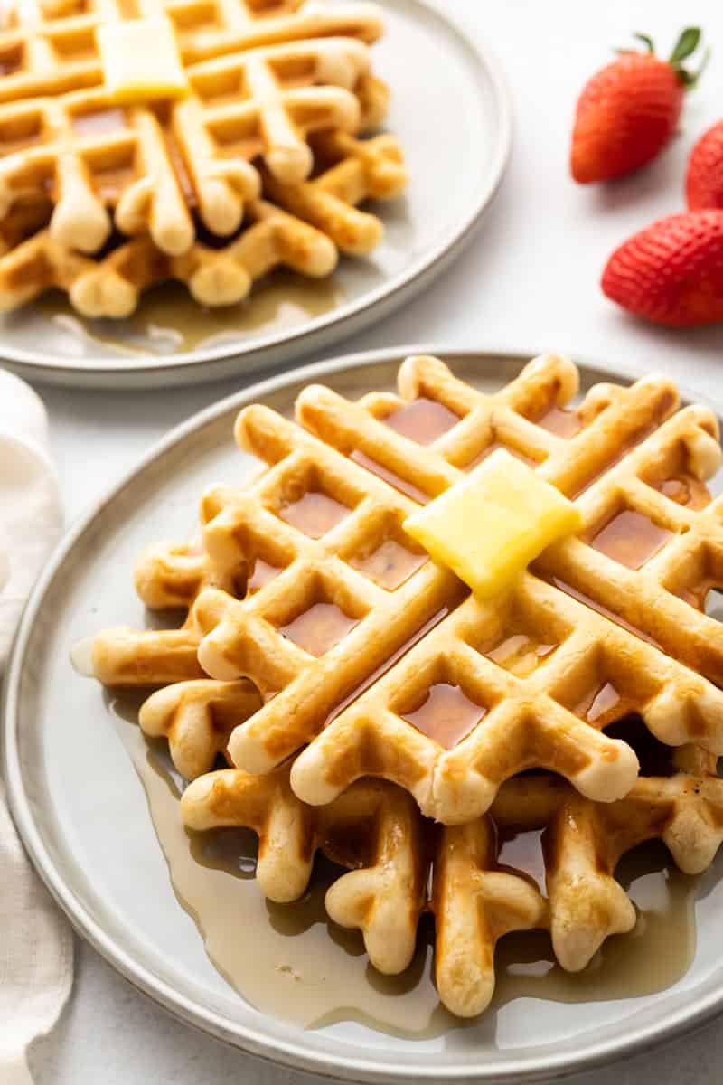 Closeup of a stack of low sodium waffles on a grey plate, covered in syrup with a pad of butter on top