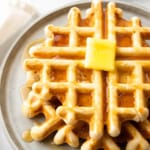 Closeup of a stack of low sodium waffles on a grey plate, covered in syrup with a pad of butter on top
