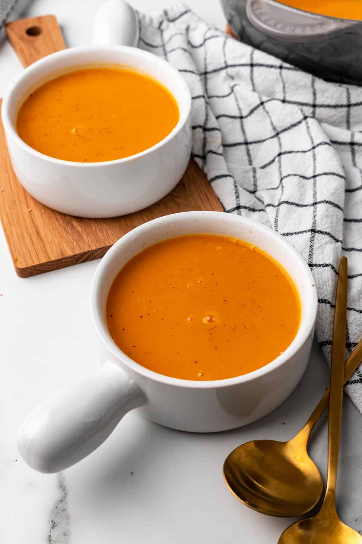 Two bowls of buttercup squash soup on a table with spoons