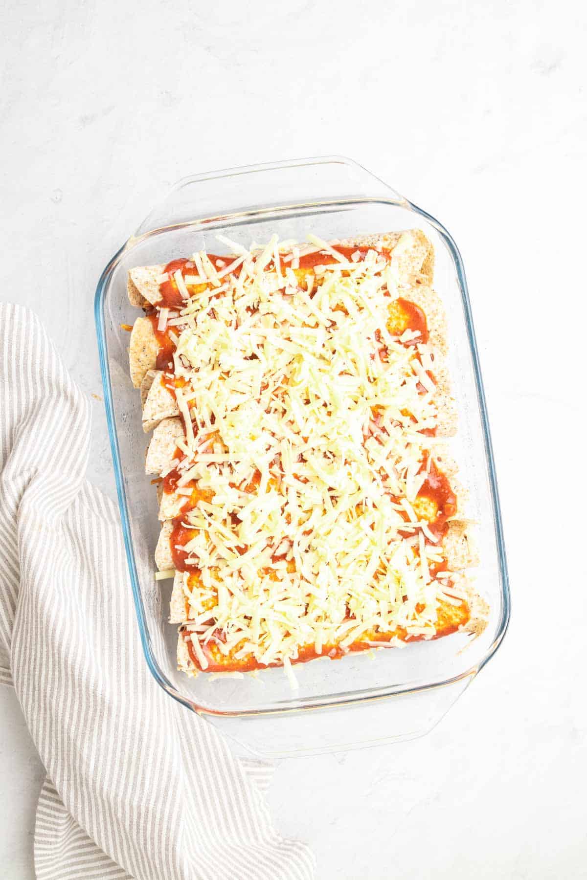 Rolled enchiladas in the baking dish topped with enchilada sauce and cheese, as seen from above