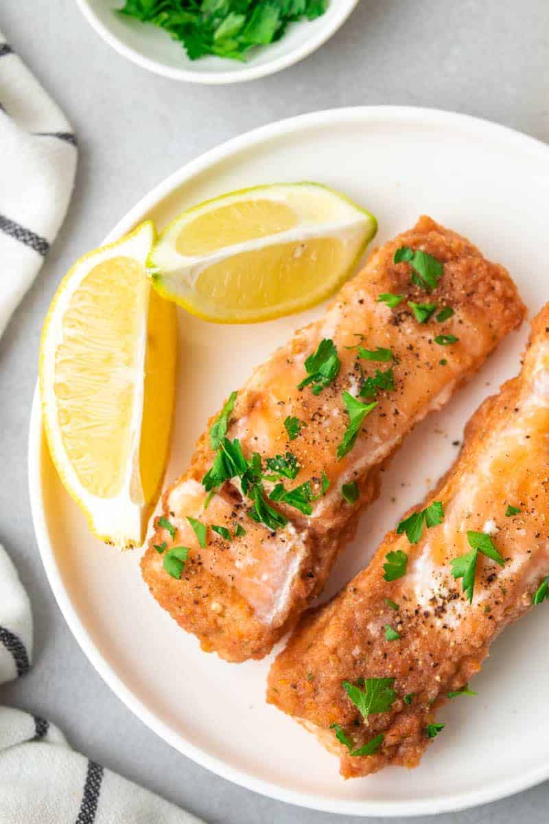 Two filets of baked salmon on a white plate next to two lemon wedges