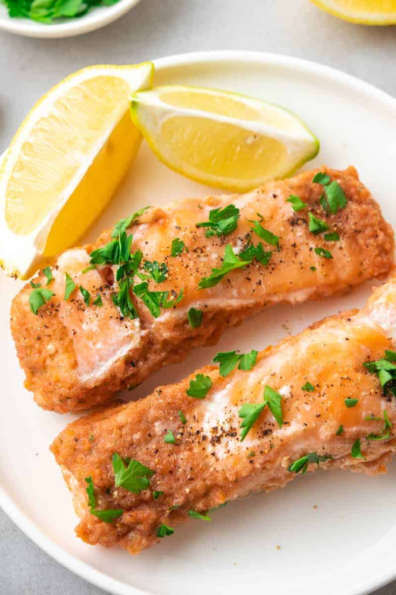 Two filets of baked salmon on a white plate next to two lemon wedges