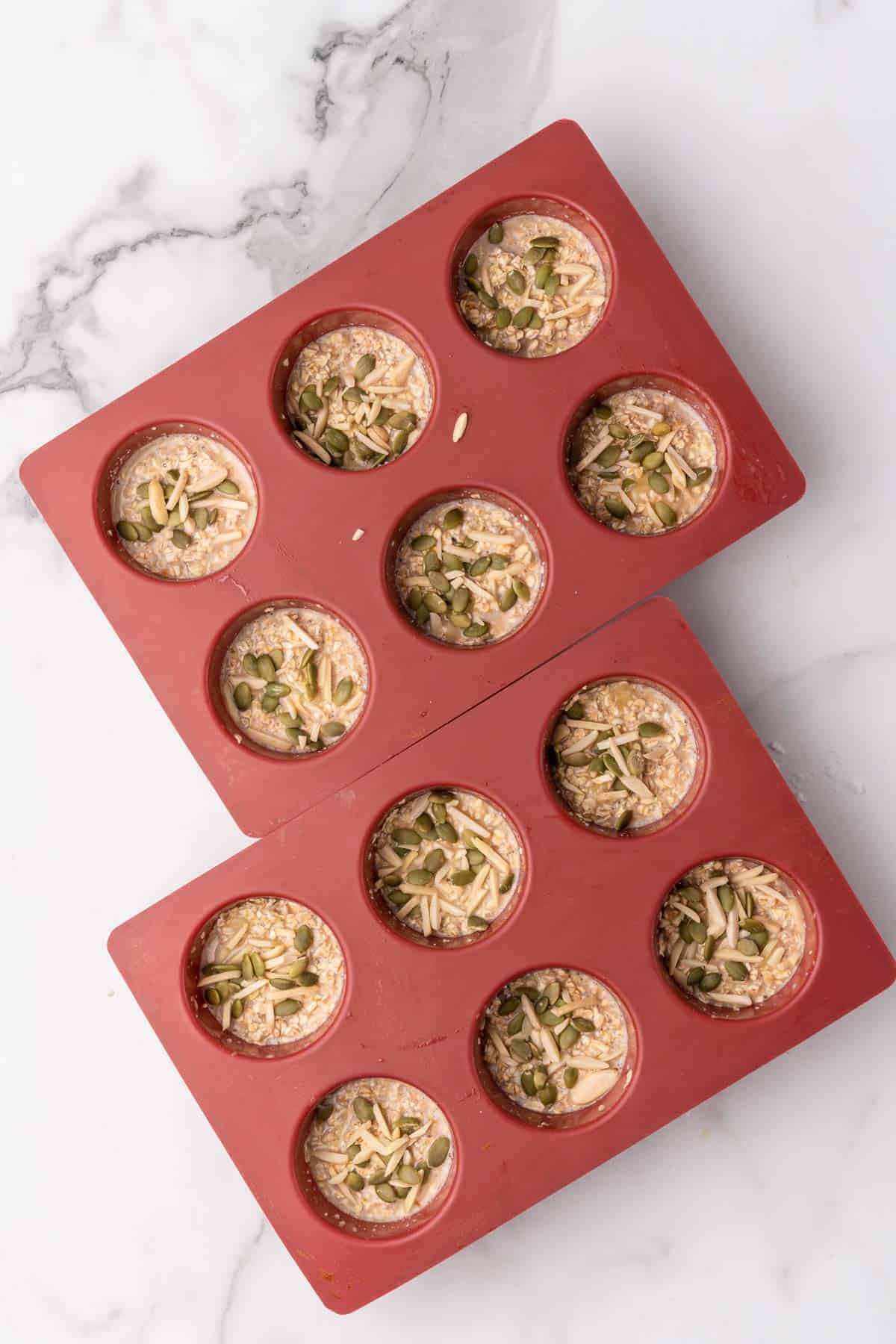 Muffin batter poured into two red silicone muffin pan with six muffins in each pan, as seen from above on a white backdrop