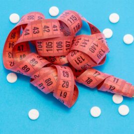 A tape measure laying on a blue background with scattered white pills