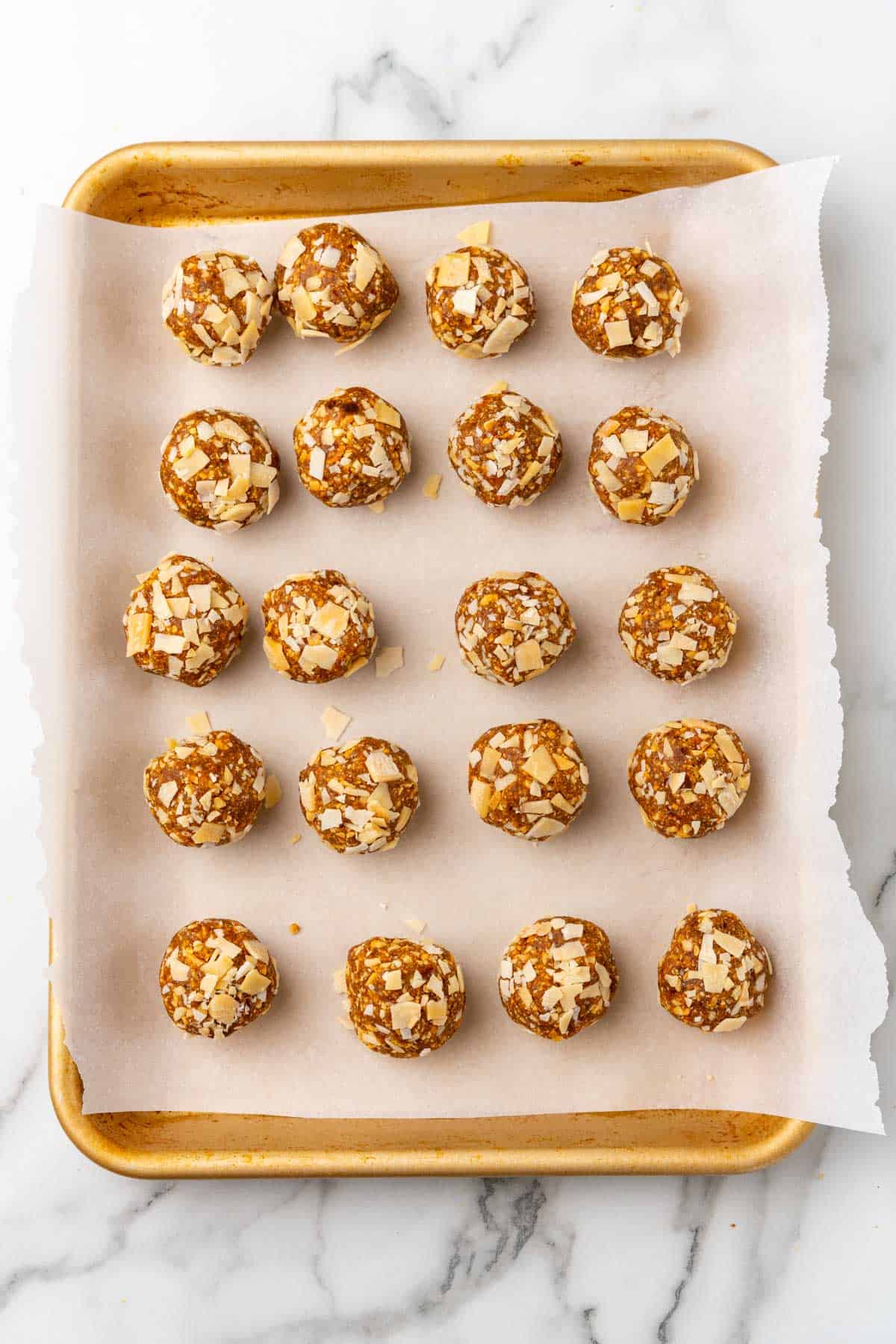 Date balls on a baking sheet lined with parchment paper, as seen from above on a white marble countertop