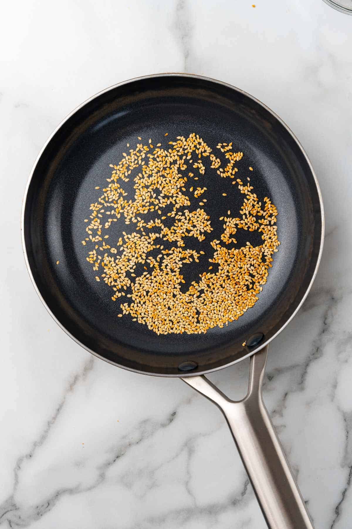 Sesame seeds in a black skillet on a white marble countertop, as seen from above