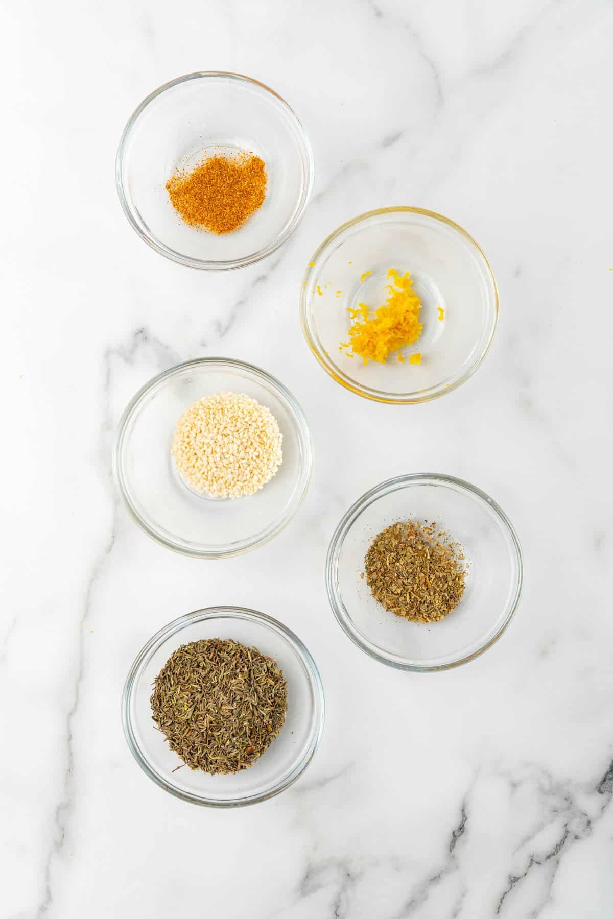Ingredients for seasoning separated into individual ramekins, as seen from above on a white marble countertop