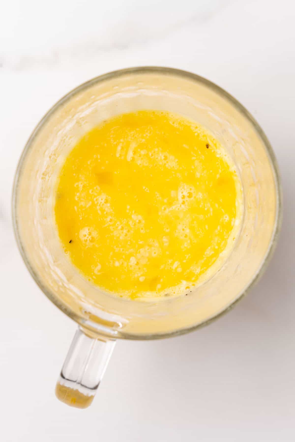 Eggs and seasoning beat together in a glass mug, as seen from above on a white background
