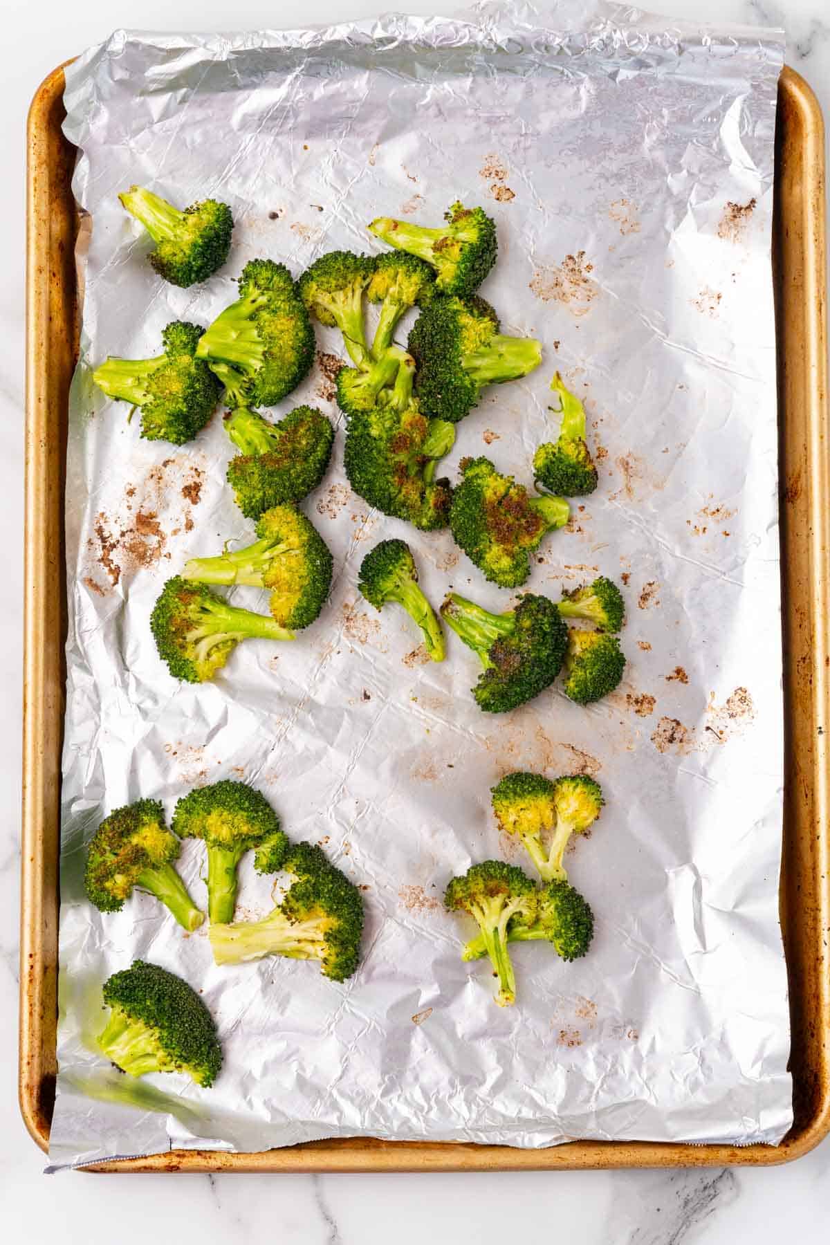 Roasted broccoli florets on a baking sheet lined with aluminum foil, as seen from above