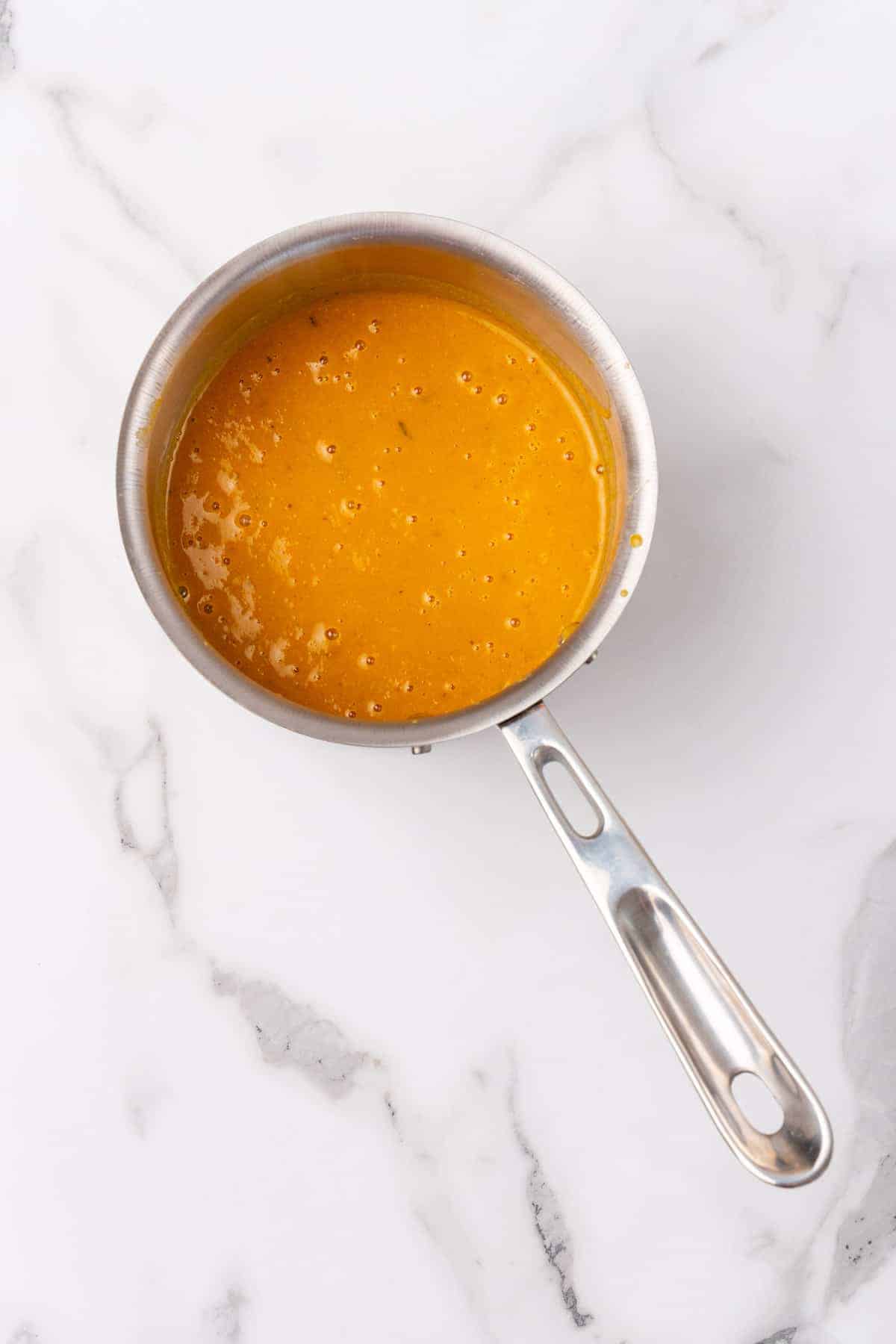 Pureed soup in a small silver saucepan on a white marble countertop, as seen from above