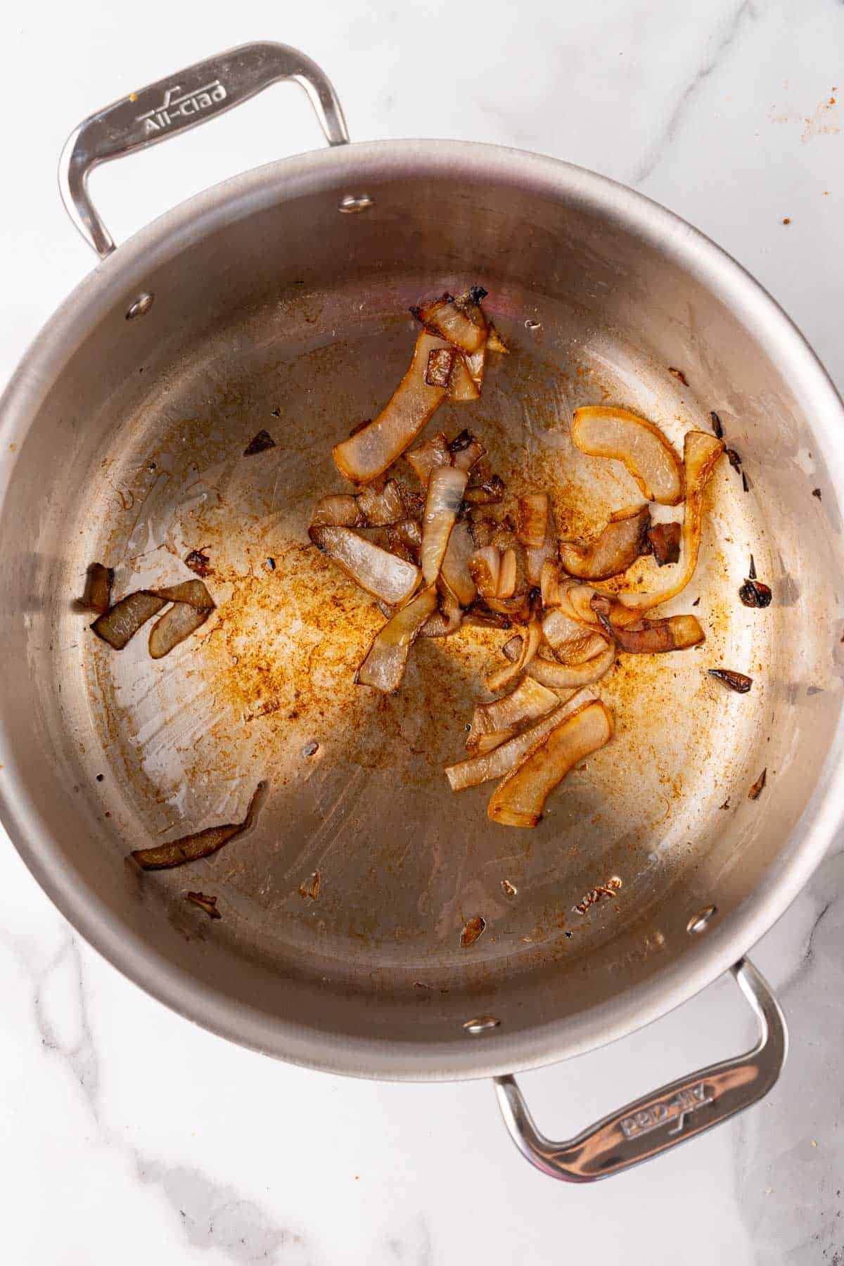 Onions caramelized in a silver saucepan, as seen from above on a white marble countertop
