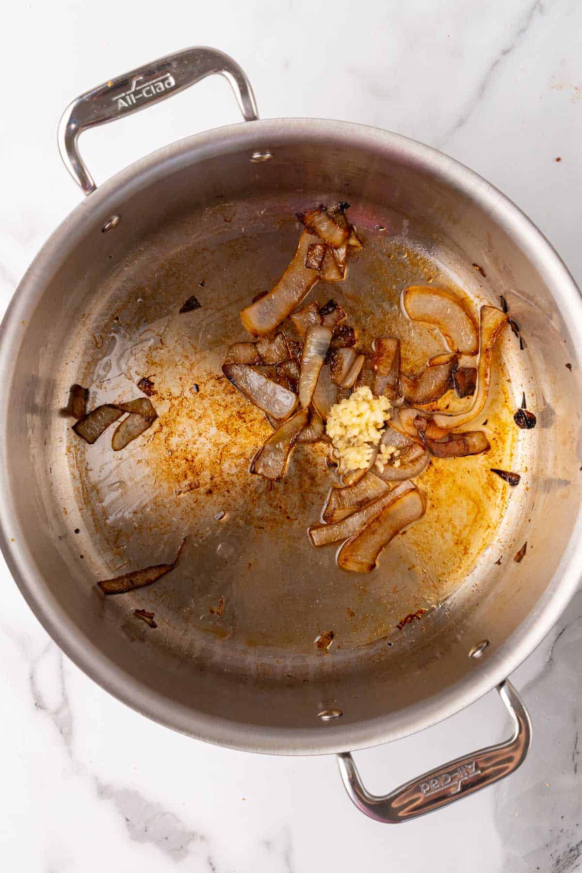 Garlic added to caramelized onions in a silver saucepan, as seen from above on a white marble countertop