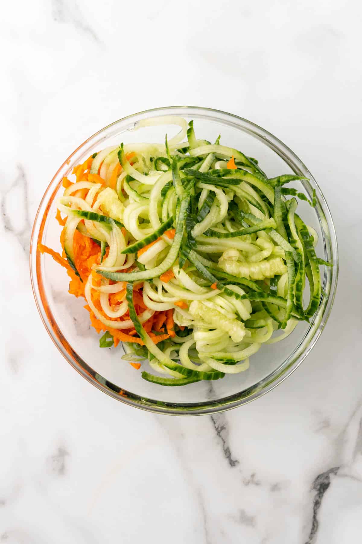 Spiralized veggies added to the glass bowl with the sauce, as seen from above, about to be mixed