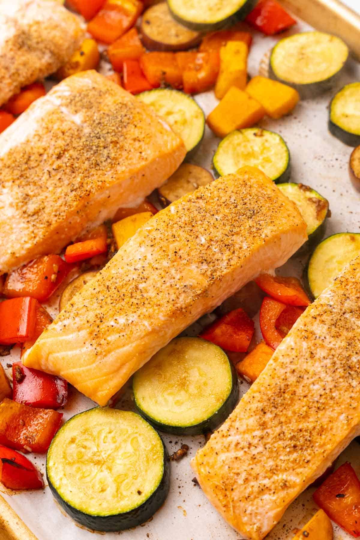 Four roasted salmon filets on top of baked veggies on a baking sheet lined with parchment paper