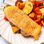 Baked salmon with roasted vegetables on a white plate on a blue checkered cloth napkin
