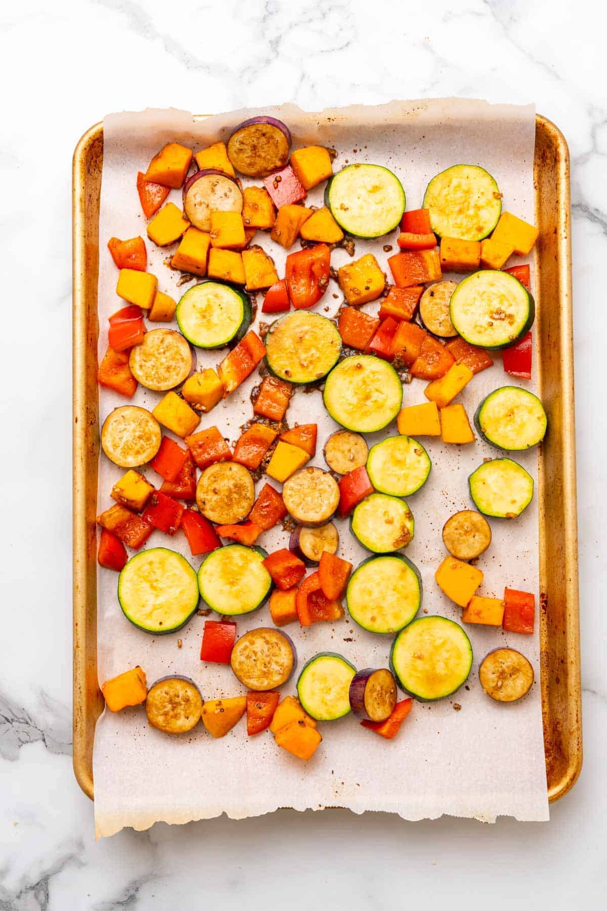 Veggies slightly roasted on a baking tray lined with parchment paper, as seen from above on a white marble countertop