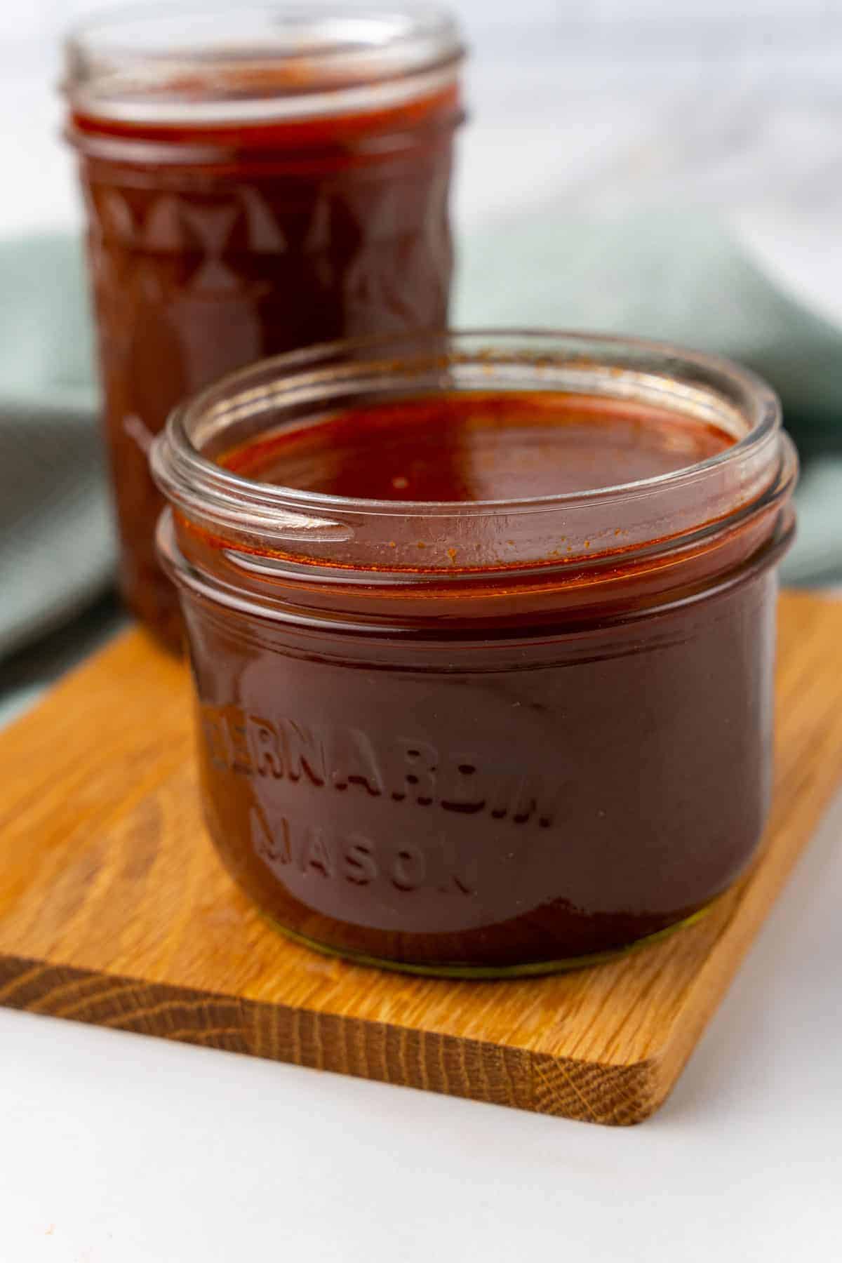 Closeup of demi-glace in a short glass mason jar on a wooden serving tray with a larger glass jar of demi-glace in the background