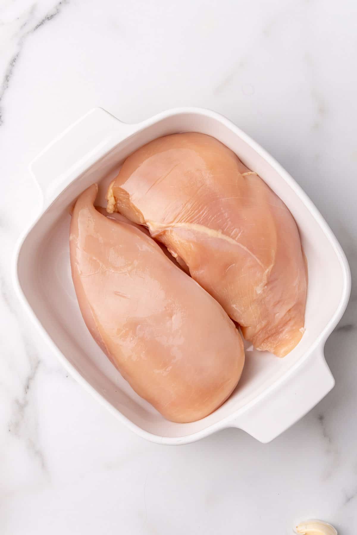 Two raw chicken breasts in a white baking dish, as seen from above
