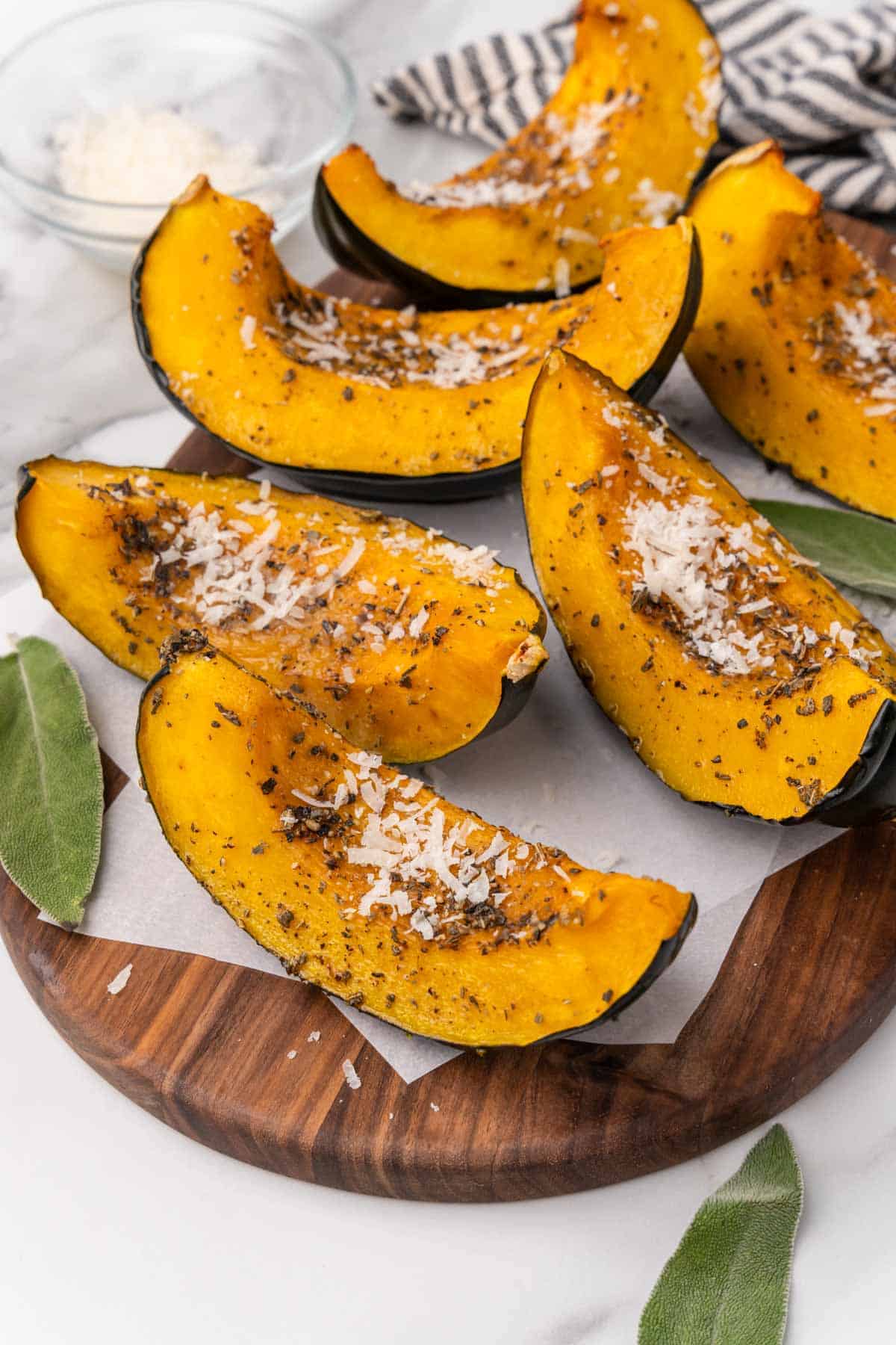 Acorn squash slices on parchment paper on an oval wooden serving tray with sage leaves placed decoratively around the slices