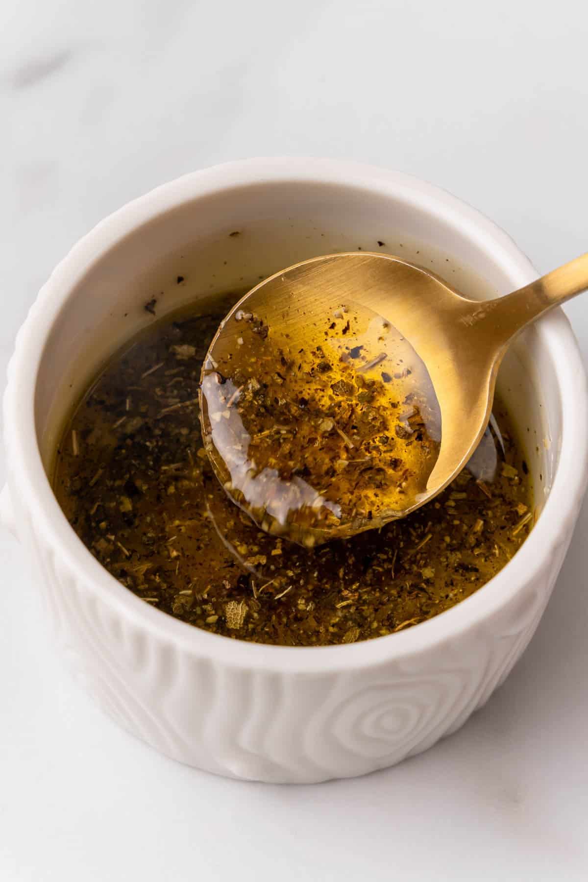 Olive oil, sage, salt, nutmeg, and pepper mixed together in a white ramekin with a gold spoon