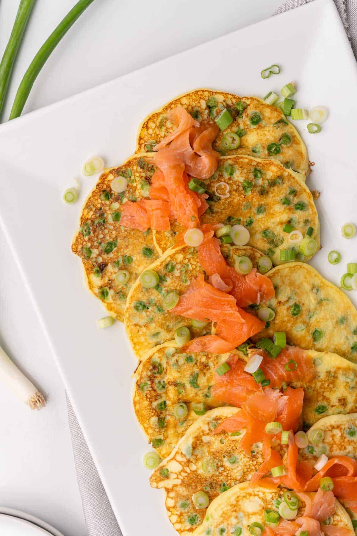 Rectanglular white platter with pancakes topped with smoked salmon and sliced scallions