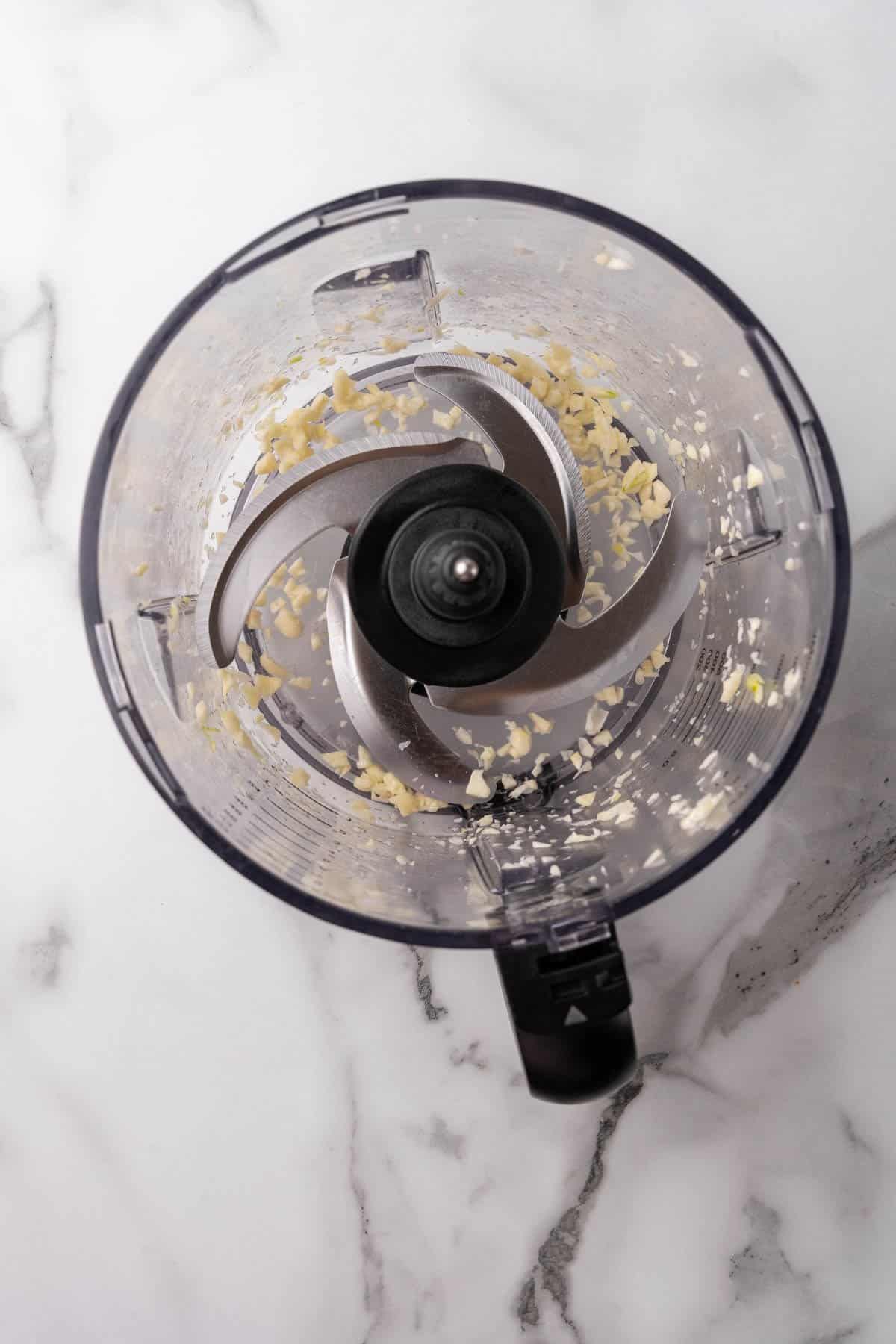 Food processor seen from above with minced garlic at the bottom