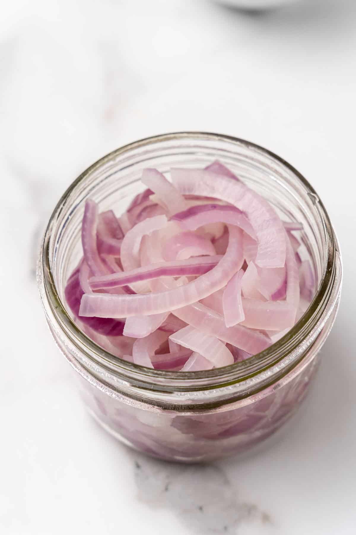 Boiled red onion slices in a glass jar on a white marble surface