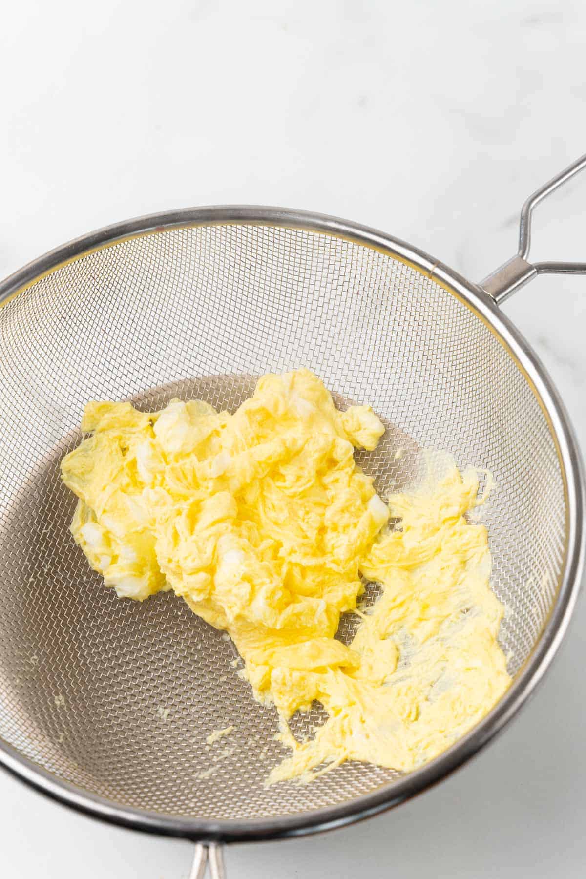 Omelet in a metal strainer over a white background