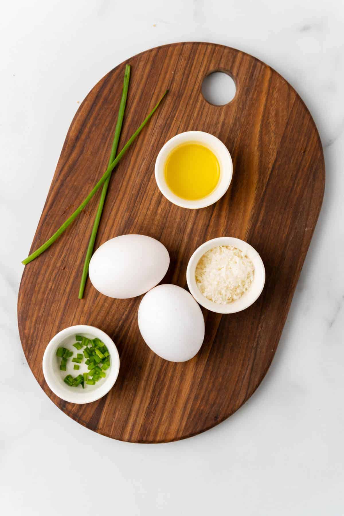 Ingredients in separate bowls and ramekins on a wooden serving tray on a white marble countertop, as seen from above