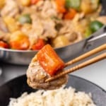 Chopsticks holding a piece of pork and bell pepper above a plate with dish and white rice; skillet in background with more