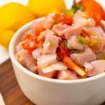Tuna ceviche in a small white bowl on a wooden serving board with two lemons and a tomato in the background