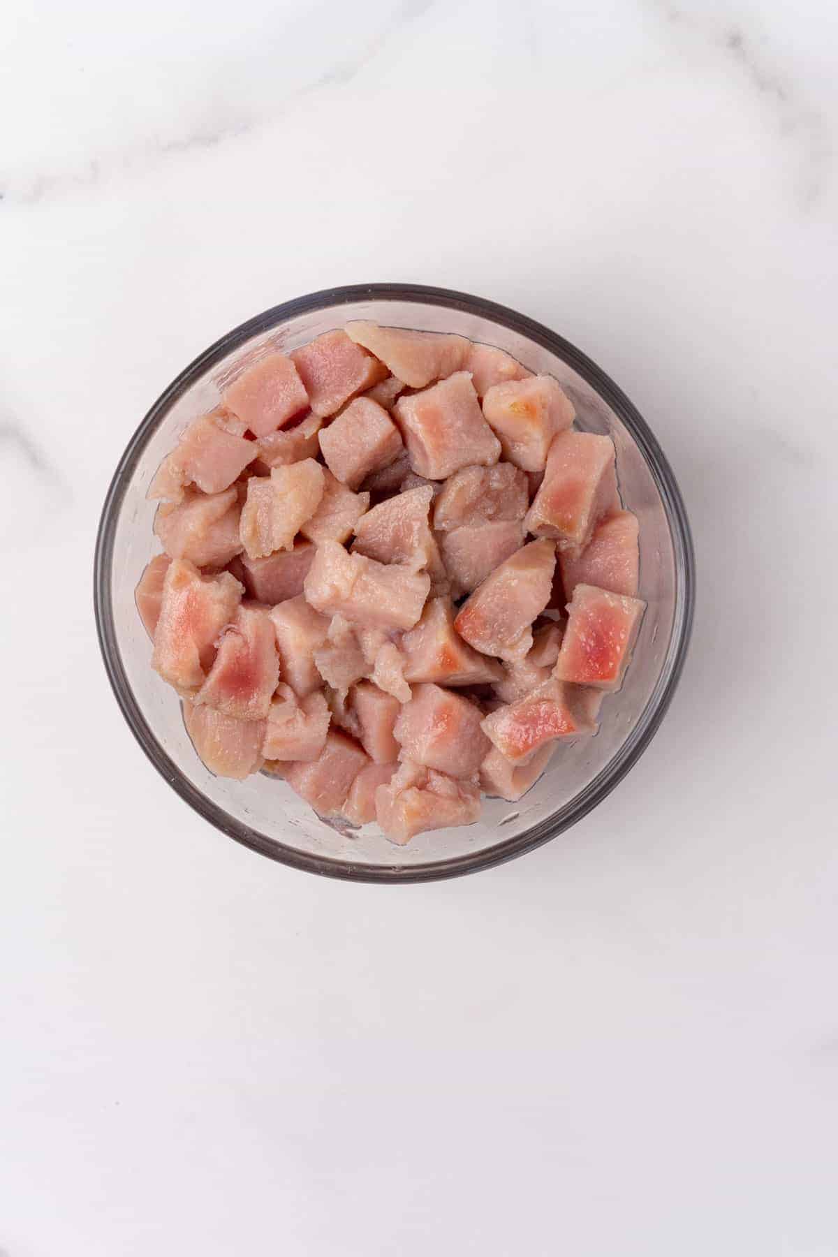 Tuna pieces, soaked and drained, in a glass bowl, as seen from above on a white marble countertop