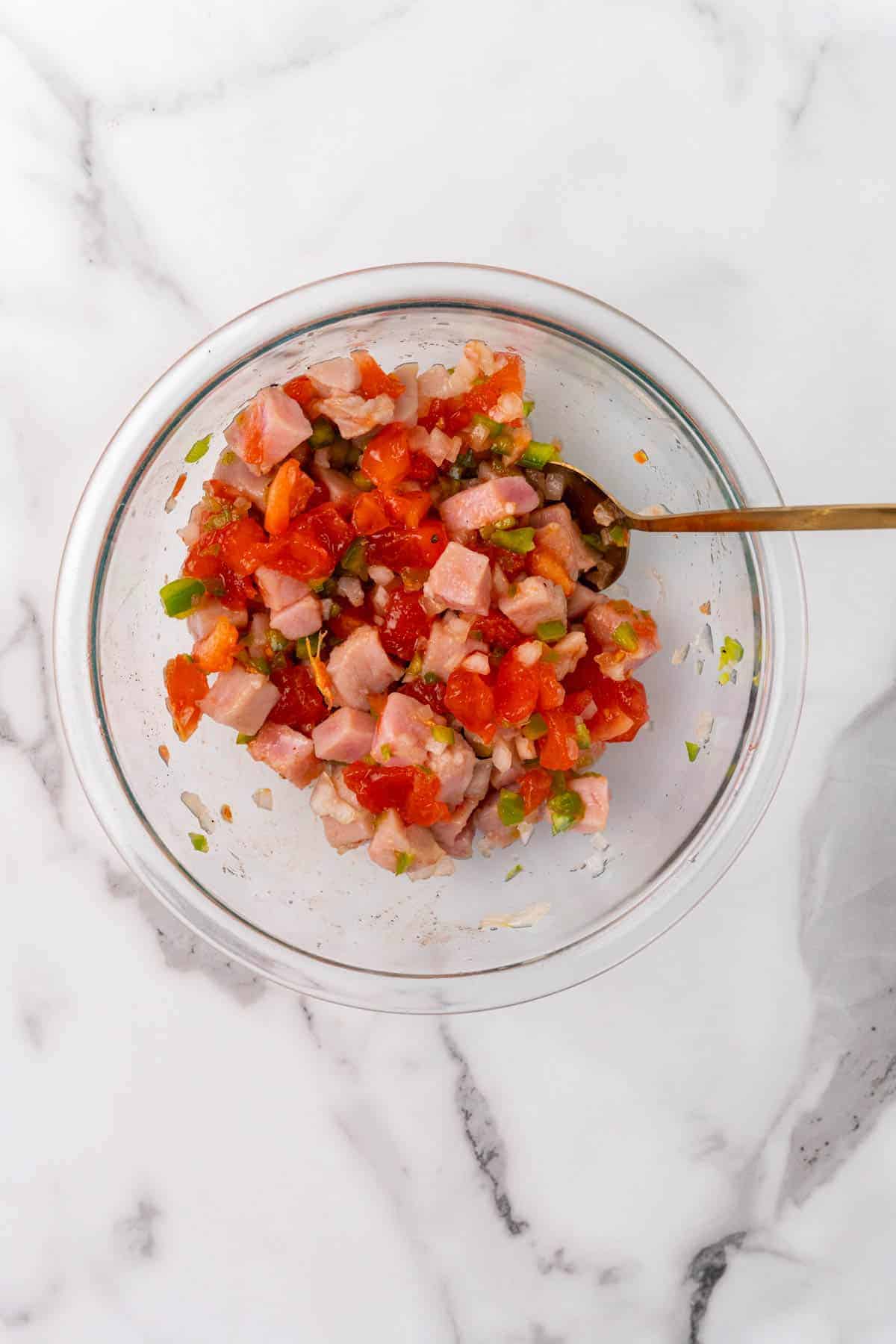 Ceviche ingredients mixed together in a glass bowl with a golden spoon, as seen from above