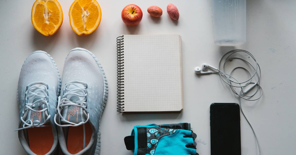 Overhead shot of a notebook, gym shoes, fruit, a smart phone, and headphones.