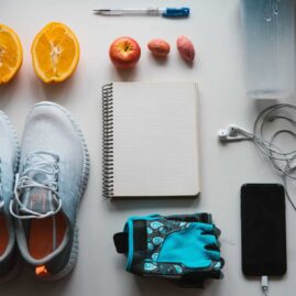 Overhead shot of a notebook, gym shoes, fruit, a smart phone, and headphones.