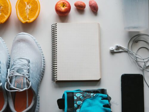 Overhead shot of a notebook, gym shoes, fruit, a smart phone, and headphones.