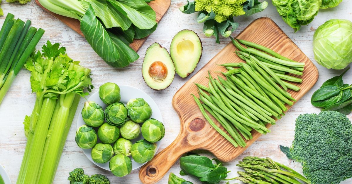 A cutting board with asparagus on it surrounded by green vegetables.