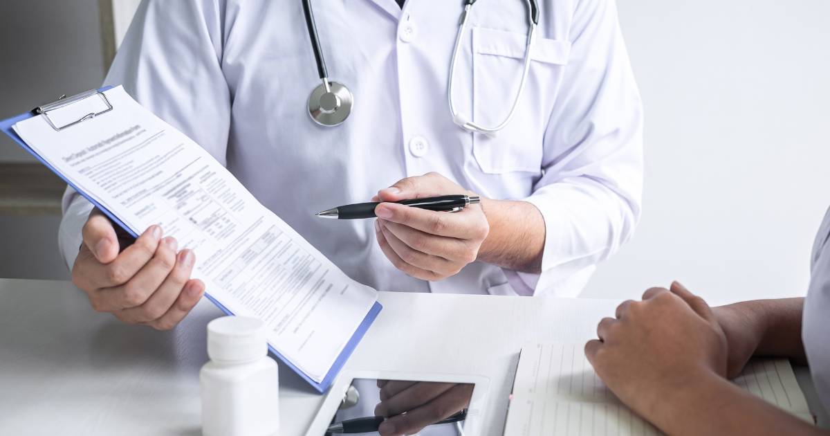 Person in white lab coat is showing someone something on a clipboard