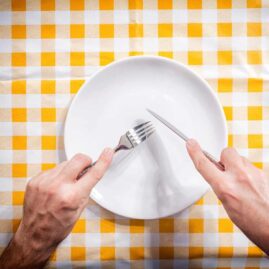 A person holds a fork and knife over an empty plate