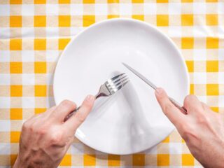 A person holds a fork and knife over an empty plate